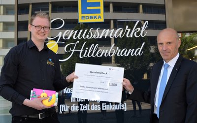 Die Übergabe des Spendenschecks fand vor dem Eingang des EDEKA in der Stettenstraße statt. Von links nach rechts: Jörg Hillenbrand und KJF Direktor Markus Mayer. Foto: KJF Augsburg/Jasmin Mächtlinger