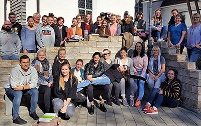 Das Bild zeigt viele junge Menschen, die auf sich auf vor und hinter einer Steinmauer zu einem Gruppenbild aufgestellt haben. 