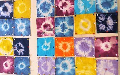 Das Bild zeigt eine Collage aus verschiedenen gebatikten Stoffquadraten in verschiedenen Farben.